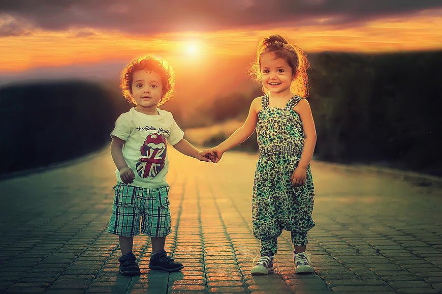 Cute children holding hands on a road at sunset