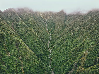 Aerial view of lush green mountain valley with waterfall and mist