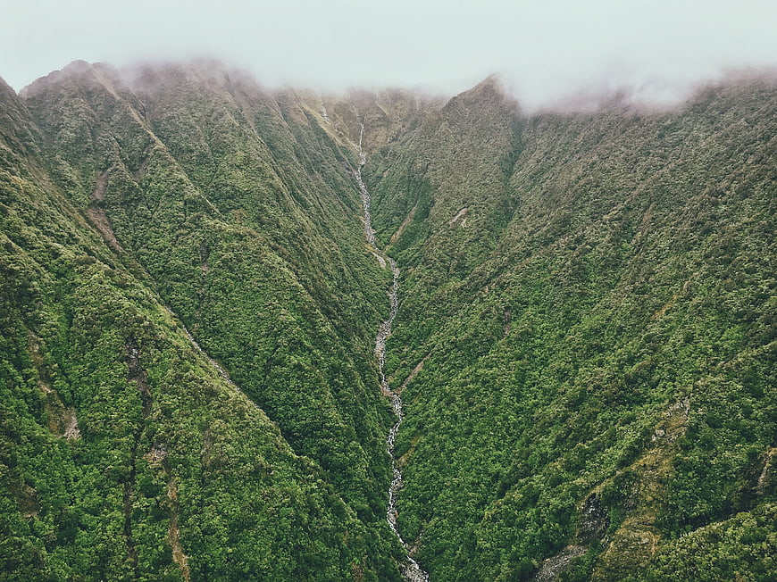 Aerial view of lush green mountain valley with waterfall and mist