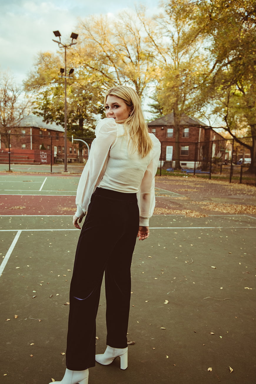 Blonde woman in white blouse and black trousers on autumn tennis court