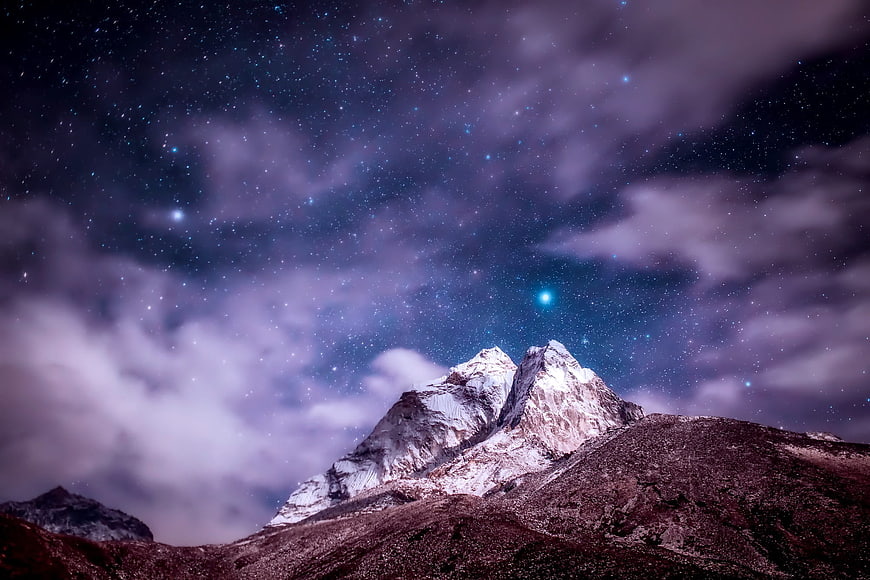 Snowy Mountain Peak Under Starry Night Sky with Clouds