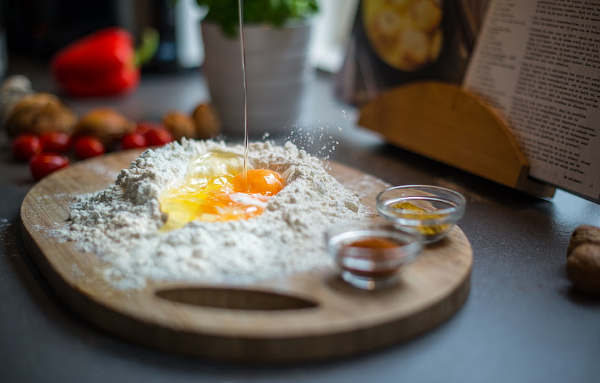 Cracking eggs into flour on wooden board with spices