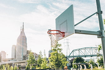 Outdoor basketball hoop with city skyline and bridge background