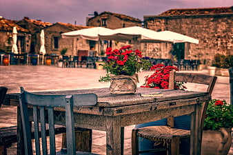 Rustic wooden table with red flowers in a Mediterranean village square