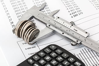 Vernier caliper measuring stack of coins on financial report