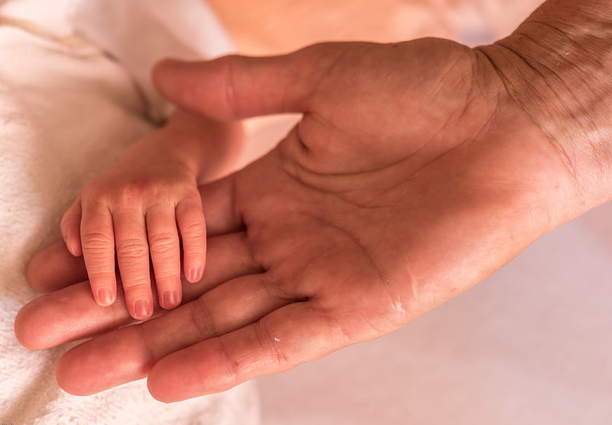 Close-up of adult hand holding baby hand on white blanket