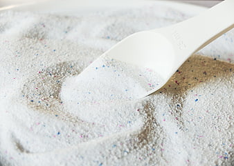 White plastic scoop in laundry detergent powder with colorful specks