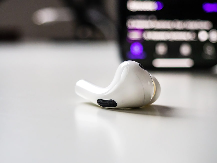 White Wireless Earbud on Desk with Blurred Phone