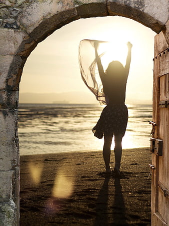 Silhouette of woman with scarf in stone archway at sunset