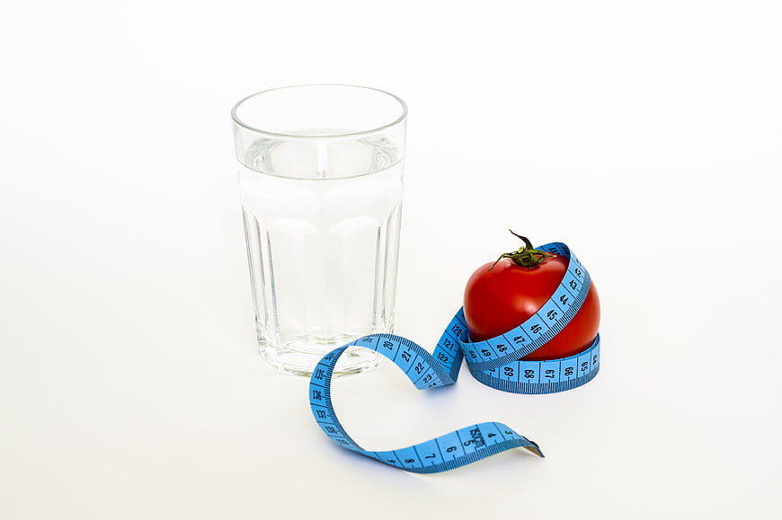 Tomato with measuring tape and glass of water on white background