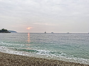 Serene sunset over pebble beach with boats on calm sea