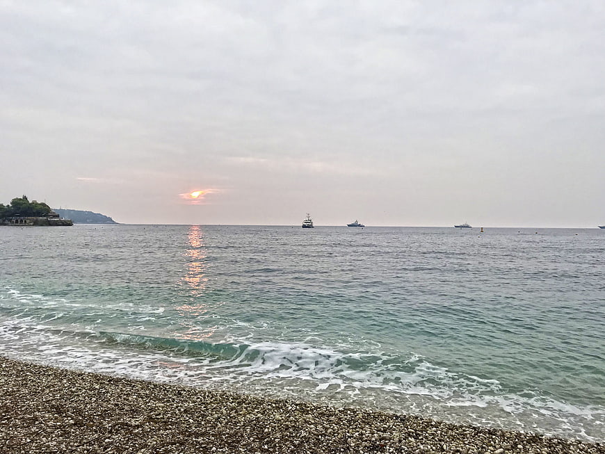 Serene sunset over pebble beach with boats on calm sea