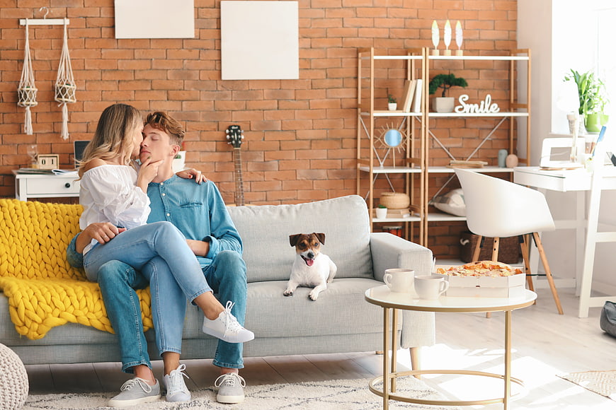 Happy couple relaxing on sofa with dog and pizza