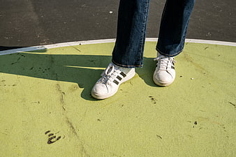 Close-up of white sneakers and jeans on green court