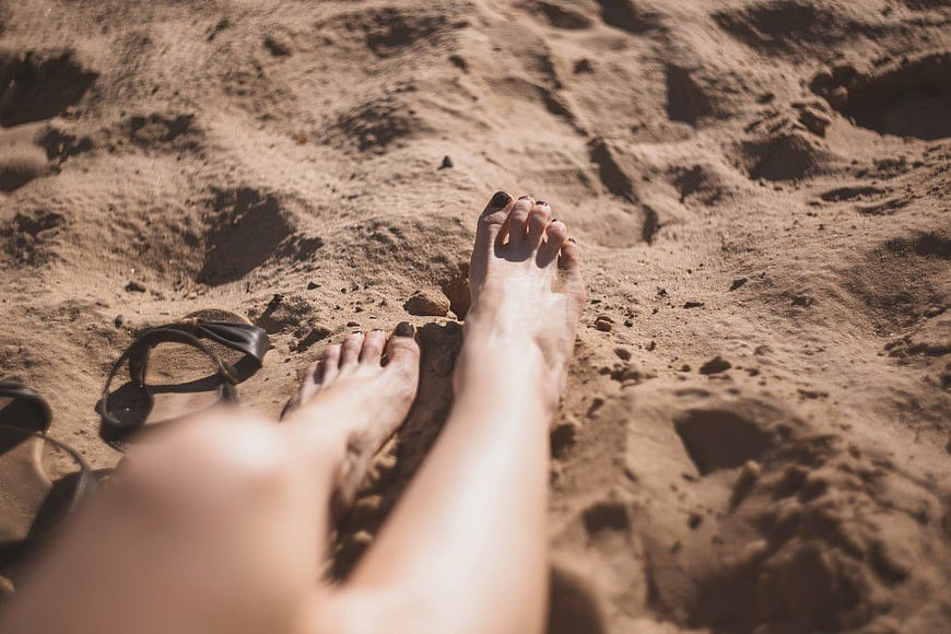 Relaxed bare feet on sandy beach with sandals