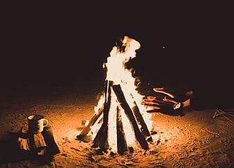 Hands warming by a campfire on a sandy beach at night