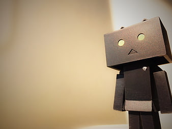 Lonely cardboard robot figure standing against a warm beige background
