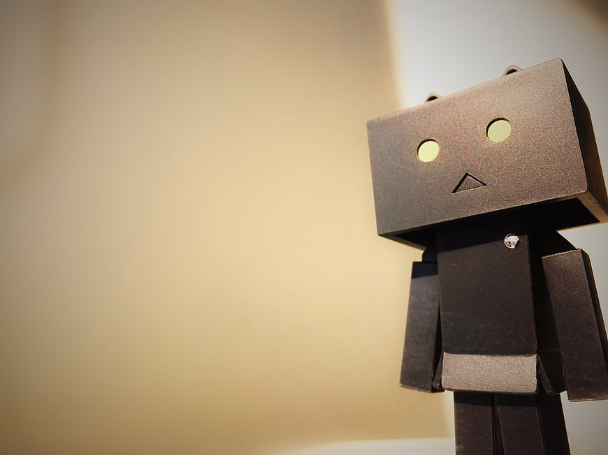Lonely cardboard robot figure standing against a warm beige background