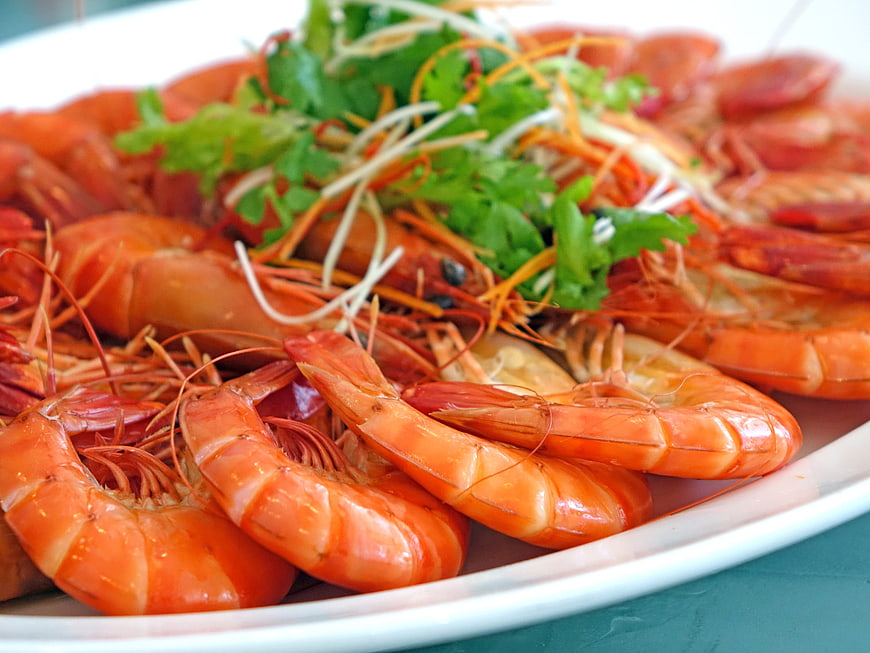 Close-up of steamed prawns with cilantro garnish on white plate