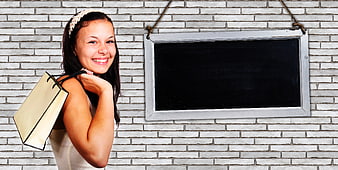 Smiling woman with shopping bag next to blackboard mockup on brick wall