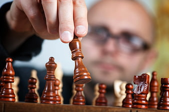 Close-up of Hand Moving Chess Piece with Blurred Player