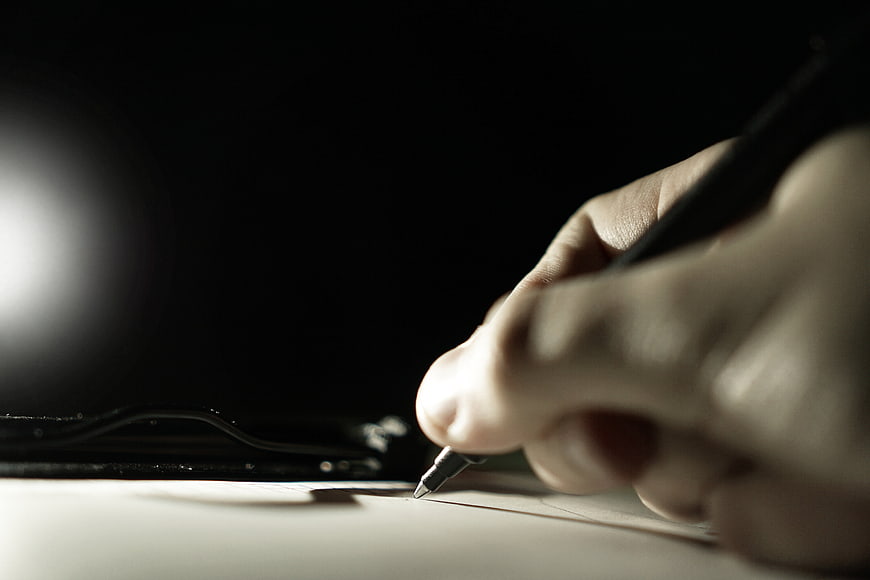 Close-up of hand writing with pen on paper in dark setting