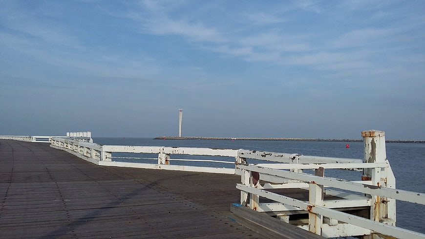 Weathered wooden pier with white railing extending over calm blue sea