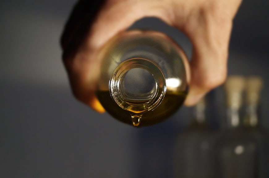 Close-up of hand holding glass bottle with golden oil drop