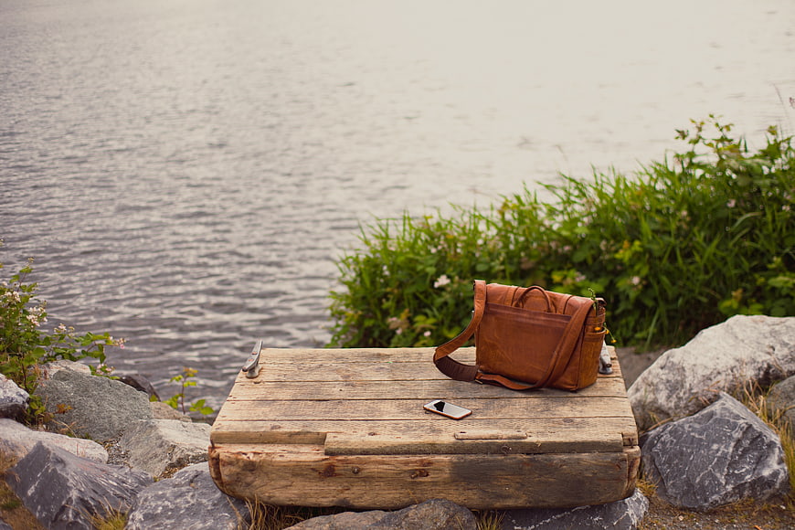 Brown leather bag and smartphone on wooden box by lake