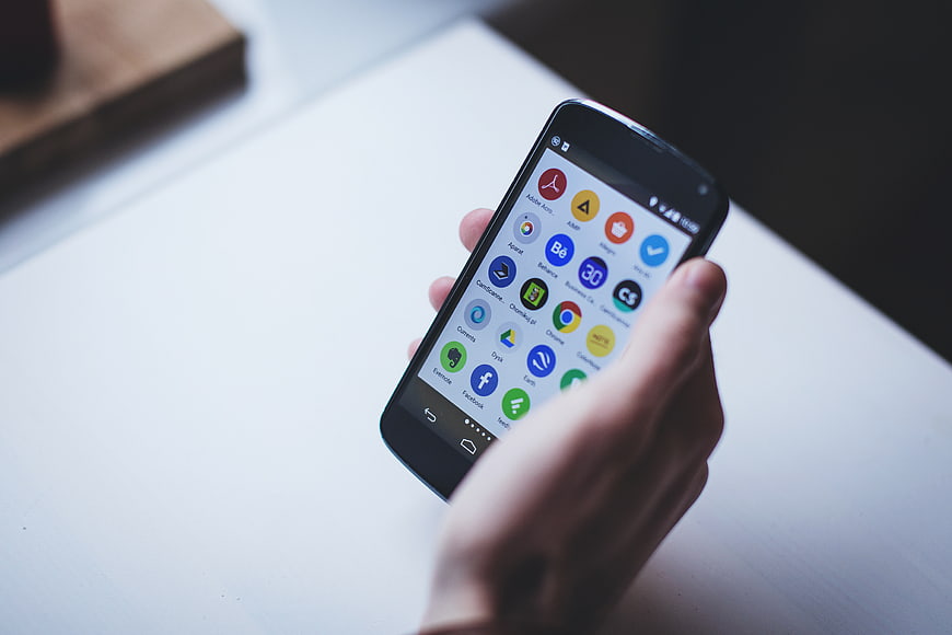 Hand holding smartphone with app icons on white desk