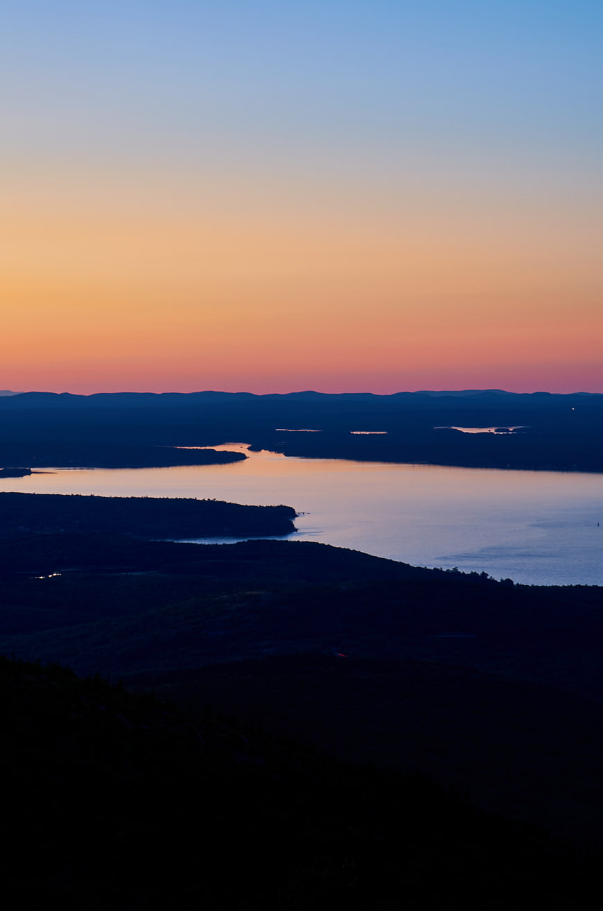 Serene Coastal Sunset Over Calm Waters and Dark Hills