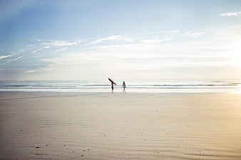 Surfers Walking on Sandy Beach at Sunset