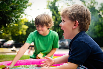 Two young boys playing in a pink inflatable pool outdoors