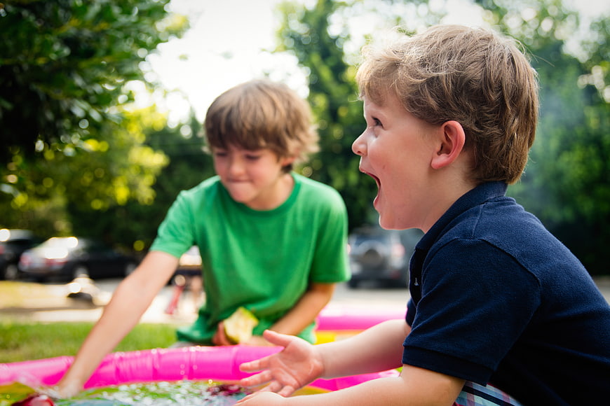 Two young boys playing in a pink inflatable pool outdoors