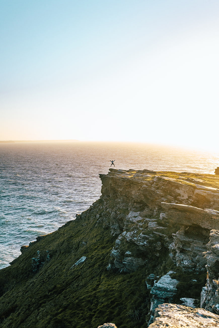 Person jumping on cliff edge at sunset over ocean