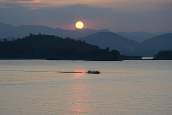 Small boat on calm lake at sunset with mountains in background