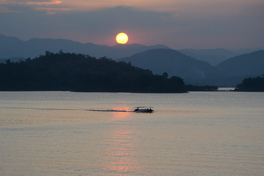 Small boat on calm lake at sunset with mountains in background