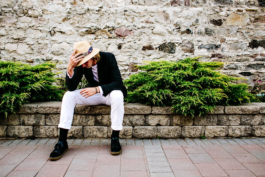 Man in Straw Hat Sitting on Stone Wall with Green Bushes