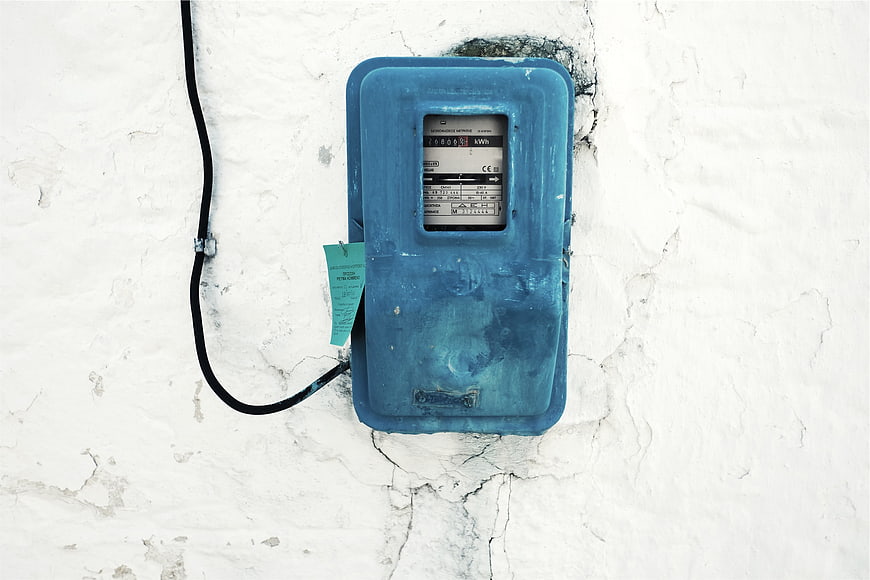 Blue electricity meter on cracked white wall