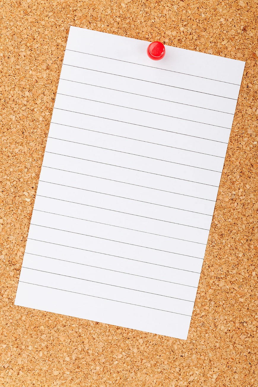 Blank lined paper pinned to cork board with red thumbtack