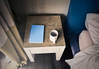 Overhead view of blue notebook and white mug on bedside table