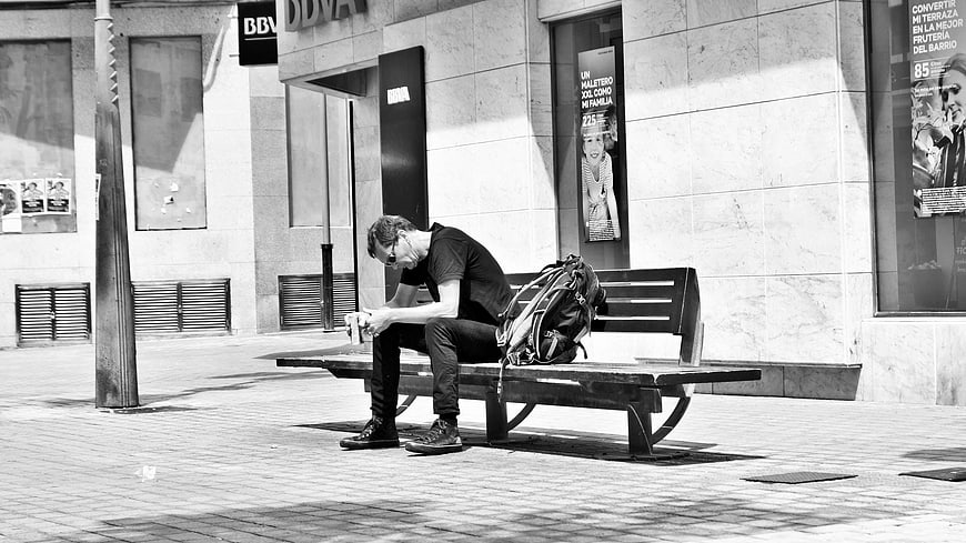 Man sitting on bench looking at smartphone in black and white