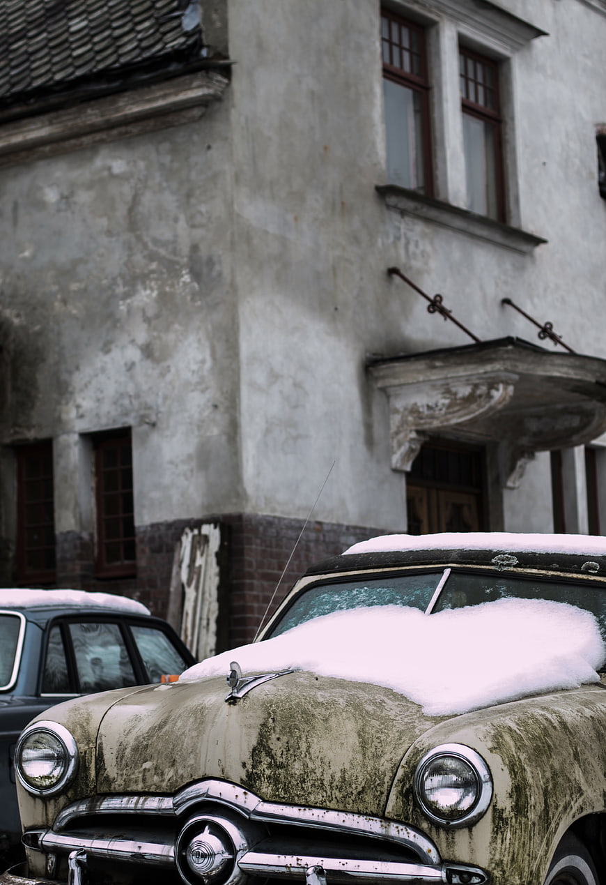 Vintage car covered in snow in front of old building