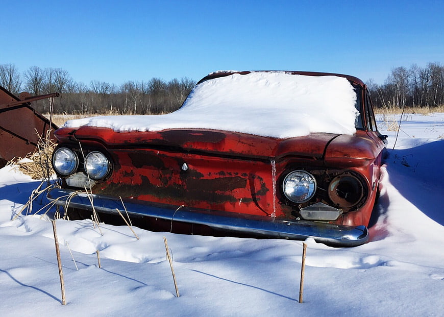 Abandoned vintage red car buried in snow