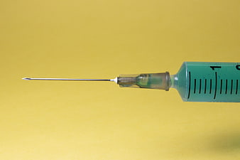 Close-up of medical syringe with green liquid on yellow background