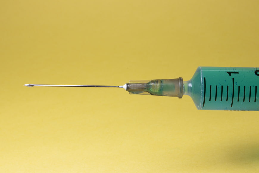 Close-up of medical syringe with green liquid on yellow background