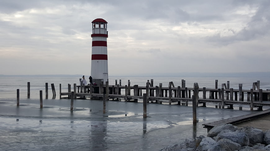 Red and white lighthouse on frozen pier in winter