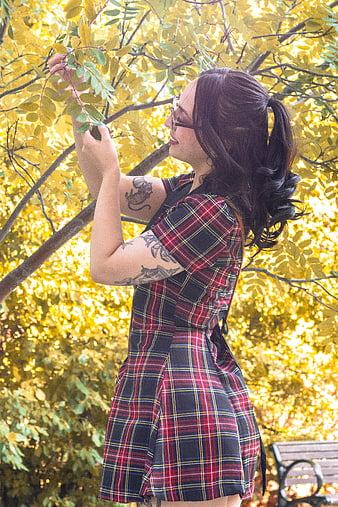 Woman in plaid dress touching autumn leaves in park
