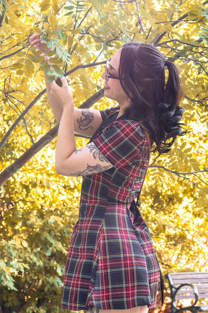 Woman in plaid dress touching autumn leaves in park