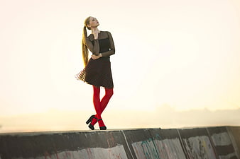 Woman in Black Dress and Red Tights on Concrete Wall